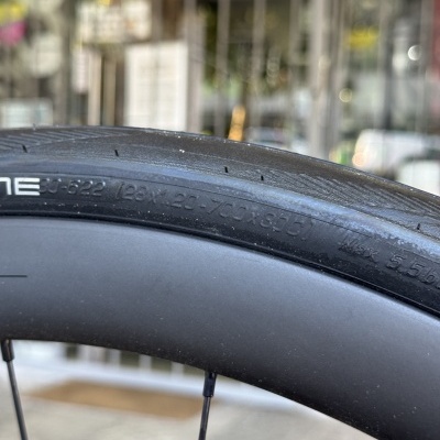 Pneu de bicicleta preto com texto das dimensões e pressão máxima numa roda preta com raios.