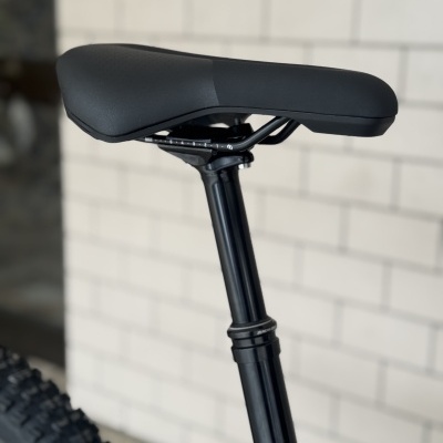 Selim de bicicleta preto com canote ajustável e parede branca ao fundo