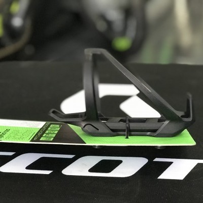 Suporte preto para garrafa de bicicleta sobre cartão verde e superfície preta com texto SCOTT em branco
