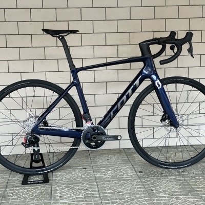Bicicleta de estrada azul escura com logo GIANT em fundo de parede de tijolos brancos