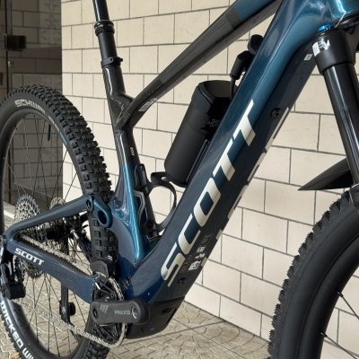 Bicicleta de montanha azul e preto com pneus Schwalbe e componentes Praxis perto de uma parede de azulejos brancos