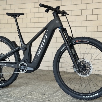 Bicicleta de montanha elétrica SCOTT preta junto a parede de tijolos claros