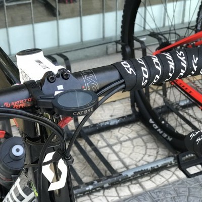 Bicicleta de estrada com guiador preto com fita SYNTACE, computador CATEYE e quadro preto e branco.