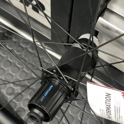 Roda de bicicleta preta com cubo preto e texto azul, etiqueta branca com texto