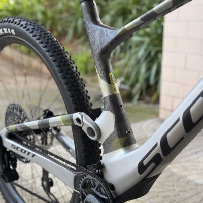 Bicicleta de montanha Scott com quadro cinzento e camuflado junto a vegetação