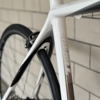 Quadro branco de bicicleta com texto TEAM e roda traseira, em fundo de azulejos brancos