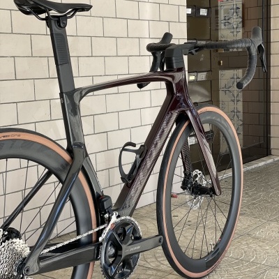 Bicicleta de estrada carbono preto e bordo com pneus bege junto a parede de tijolos
