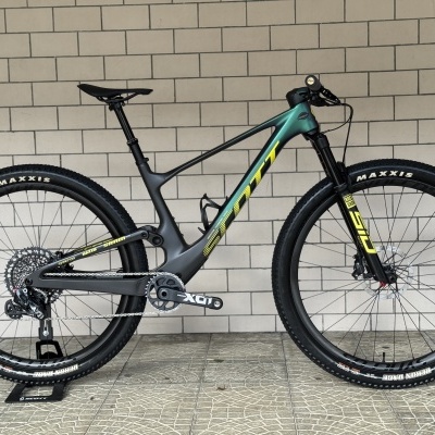 Bicicleta de montanha Scott verde e cinza com detalhes amarelos encostada numa parede de azulejos cinzentos.