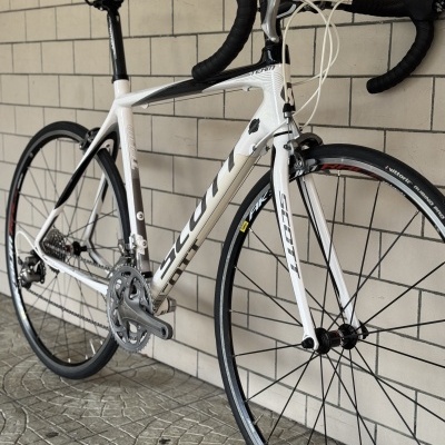 Bicicleta de estrada Scott branca e preta encostada a parede com azulejos cinza.