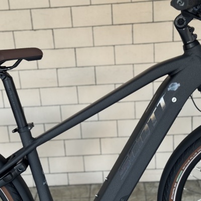 Bicicleta preta com assento castanho e pneu Schwalbe Active Plus encostada a uma parede de azulejos