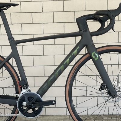 Bicicleta de estrada preta com pneus castanhos encostada a muro de tijolos claros