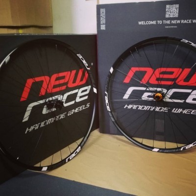 Rodas de bicicleta pretas com aros de fibra de carbono e caixas ao fundo com texto da marca New Race