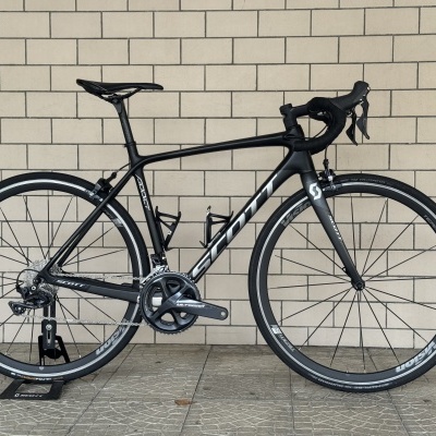 Bicicleta de estrada preta com rodas Vision TEAM 35 e componentes Shimano Ultegra encostada a parede de tijolos clara.