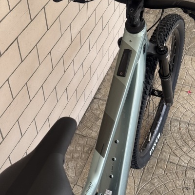 Bicicleta elétrica de montanha cinza com guiador preto e ecrã Bosch encostada a uma parede de azulejos.