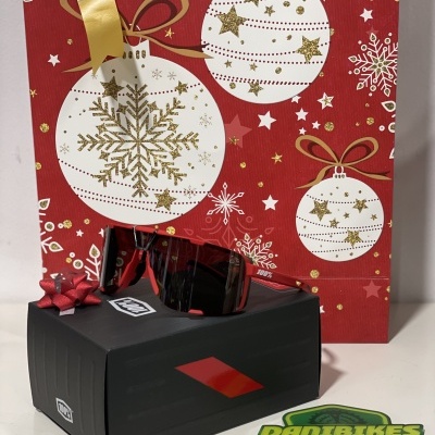 Óculos de sol vermelhos sobre caixa preta com saco de presente natalício ao fundo