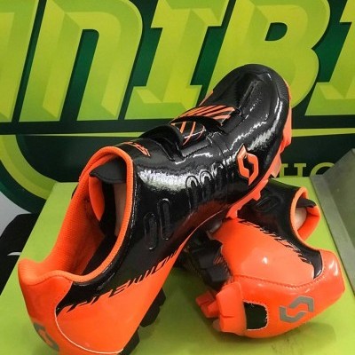 Sapatilhas de futebol preto e laranja com sola cravada sobre superfície verde