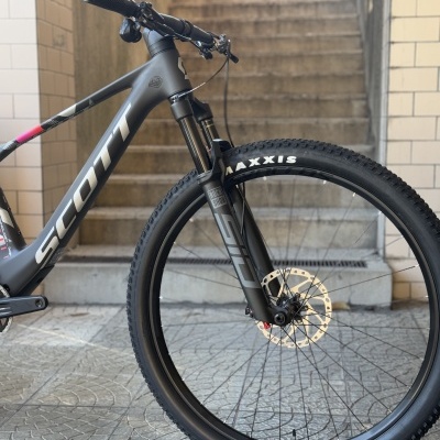 Bicicleta de montanha preta com pneus MAXXIS e suspensão FOX em frente a escadas