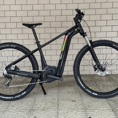 Bicicleta elétrica de montanha preta com pneus Schwalbe Nobby Nic e motor integrado num chão de mosaico claro e parede de tijolos.