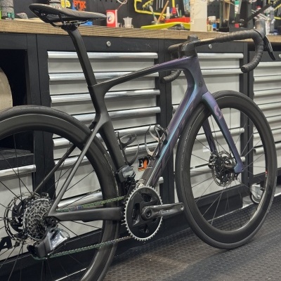 Bicicleta de estrada carbono preta e roxa numa oficina com ferramentas e armários