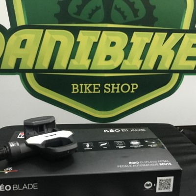 Pedal para bicicleta preto e branco KÉO BLADE sobre caixa preta com logo DANIBIKES BIKE SHOP ao fundo