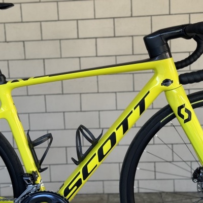 Bicicleta de estrada amarela fluorescente SCOTT com detalhes a preto e fundo de azulejos cinzentos