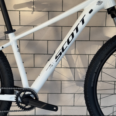 Bicicleta branca SCOTT com quadro metálico e pneus pretos, encostada em parede de azulejos brancos