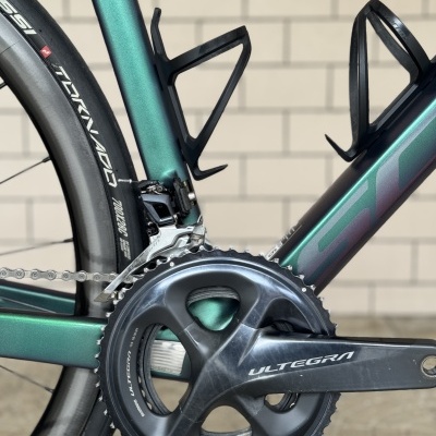 Close-up do pedivela Ultegra e pneu preto com texto branco numa bicicleta com quadro verde metálico