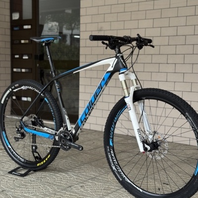 Bicicleta de montanha preta, branca e azul com suspensão RockShox e pneus Continental e Maxxis