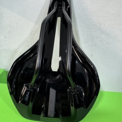 Sela de bicicleta preta com estrutura metálica e recorte central sobre superfície verde