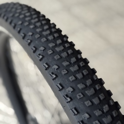 Pneu de bicicleta preto com relevo quadrado e raios metálicos ao fundo