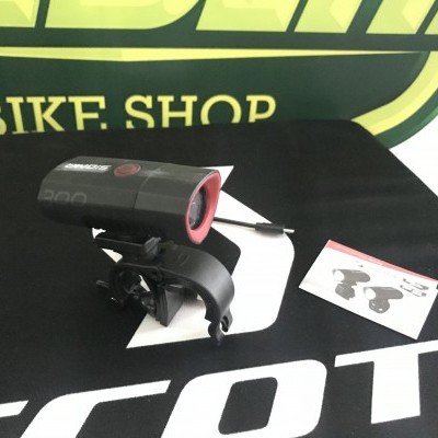 Luz frontal preta para bicicleta com detalhes vermelhos sobre superfície com letras