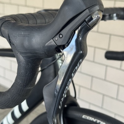 Punho e manete de bicicleta de corrida preto com marcações Shimano e Supreme, em ambiente com parede branca azulejada.