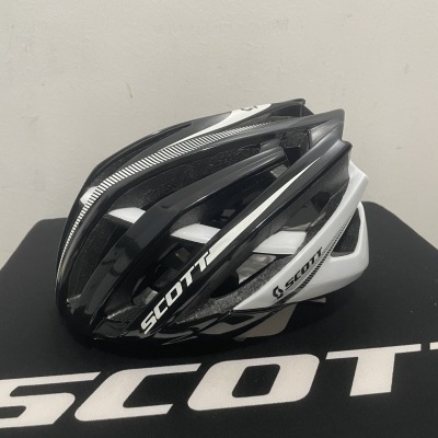 Capacete preto, branco e cinzento da marca SCOTT sobre superfície preta com texto