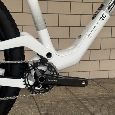 Parte inferior branca de uma bicicleta com pedaleira preta Shimano e parede de azulejos ao fundo