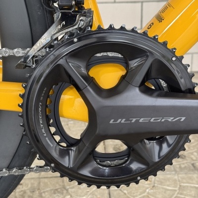 Peça de bicicleta Shimano Ultegra preta em quadro amarelo sobre piso de cimento.