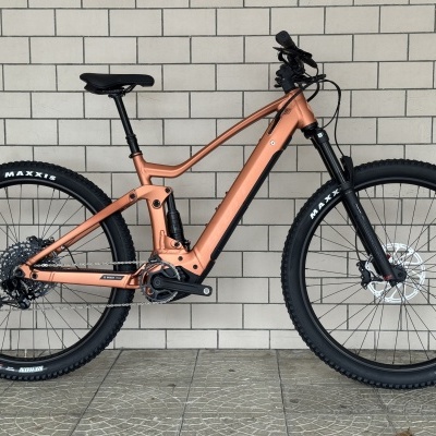 Bicicleta montanha elétrica cobre com pneus pretos Maxxis e suspensão preta