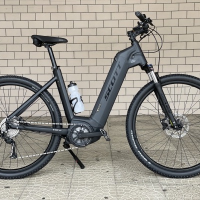 Bicicleta elétrica Scott cinzenta mate encostada numa parede de tijolos