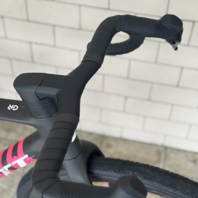 Guiador preto de bicicleta de estrada com mudanças eletrônicas, quadro cinzento e rosa, parede de tijolos brancos