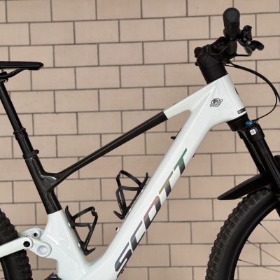 Bicicleta de montanha branca e preta marca SCOTT encostada numa parede de azulejos beje