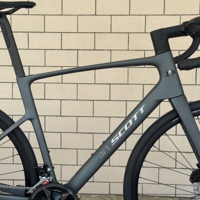 Bicicleta de estrada cinzenta com guiador preto e rodas finas, texto SCOTT no quadro.