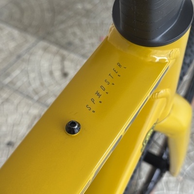 Quadro superior amarelo de bicicleta com texto SPEDSTER GRAVEL e dois parafusos pretos