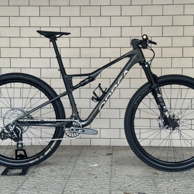 Bicicleta de montanha preta com pneus Maxxis e suspensão Fox em fundo de tijolo claro