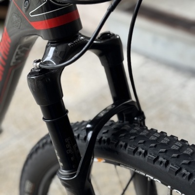 Bicicleta com suspensão dianteira preta e pneus com cravos, detalhes em vermelho e cinzento.