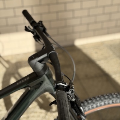 Bicicleta com guiador preto e quadro cinzento escuro junto a parede de tijolos clara