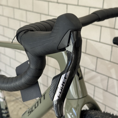 Guiador de bicicleta preto com alavanca SRAM FORCE em quadro verde claro junto a parede de azulejos brancos