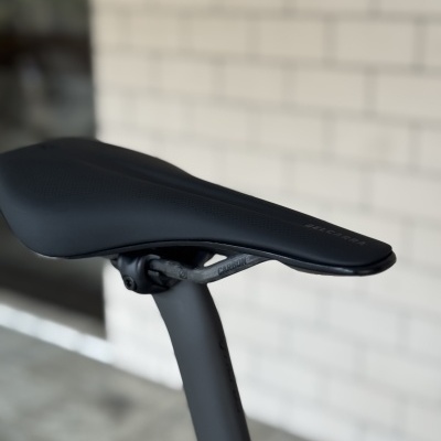 Selim de bicicleta preto com texto BELGARRA e estrutura de carbono com texto CARBON em fundo de parede branca