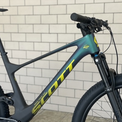 Bicicleta de montanha SCOTT preta com detalhes amarelos junto a uma parede de tijolos claros