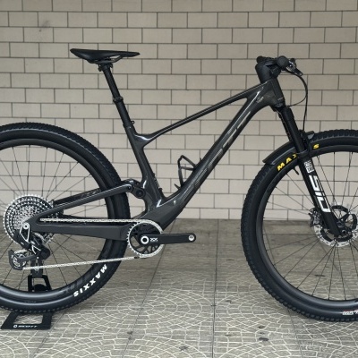 Bicicleta de montanha cinza metálico com pneus pretos Maxxis e suspensão Rock Shox