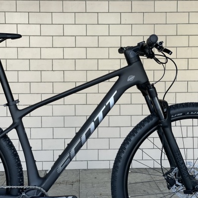 Bicicleta de montanha preta com letras SCOTT em fundo de ladrilhos brancos