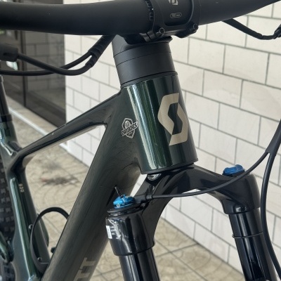 Bicicleta com quadro verde escuro, guiador preto com inscrição 760 mm e garfo dianteiro preto